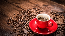 条纹木板上的咖啡豆与热气腾腾的红色咖啡杯