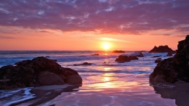 桃红色日落下的海洋岩石海滩