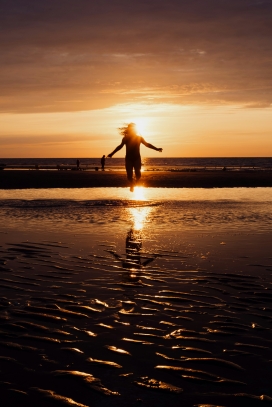 日落下海滩跳跃的女郎