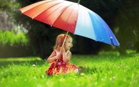坐在绿色草坪上手打五彩雨伞的小女孩