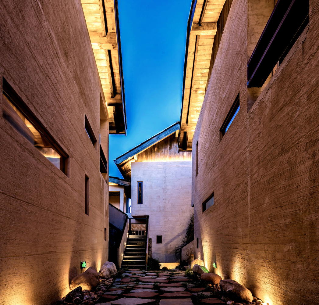 言・意的建筑由六栋小楼以及一栋老藏房组成,前厅大堂及餐厅所在的两栋建筑,视觉上犹如漂浮在空中,整个建筑群高低起伏、相互交错,楼与楼之间以走廊桥梁相连接。民宿共计15间客房,还设有大堂,餐厅和茶室;每间客房都设有入户的独特设计,展现出东方新禅意之美,同时也给客人带来了私密的体验。其中一栋建筑完整保留了原始藏式结构,徐老师提取了当地的藏式元素融进建筑及室内设计中,窗的设计也采用借景的手法,客人在房间透过窗户便能看到窗外美好的景致,蓝天白云,日出日落,大自然馈赠的美景犹如挂画一般,透过这些窗户展现在眼前。