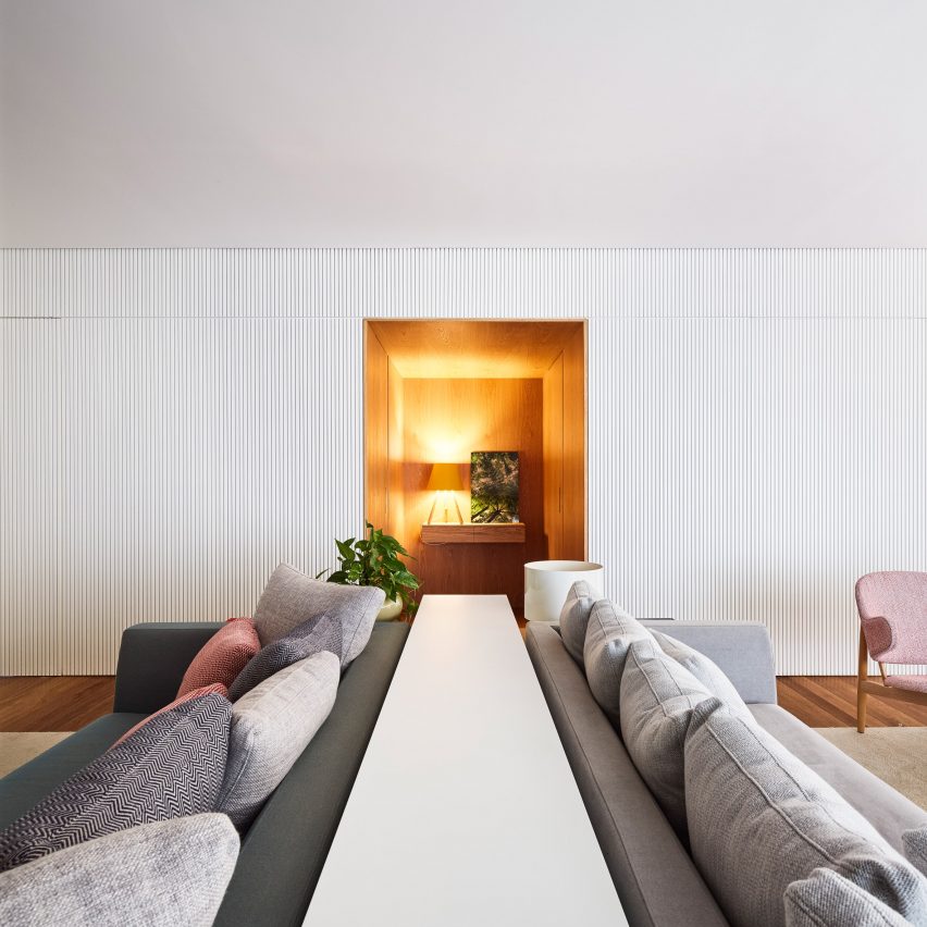 整个后墙都覆盖着镶有垂直凹槽的白色面板,这些包围木门的电梯门廊和隐藏存储区的门口