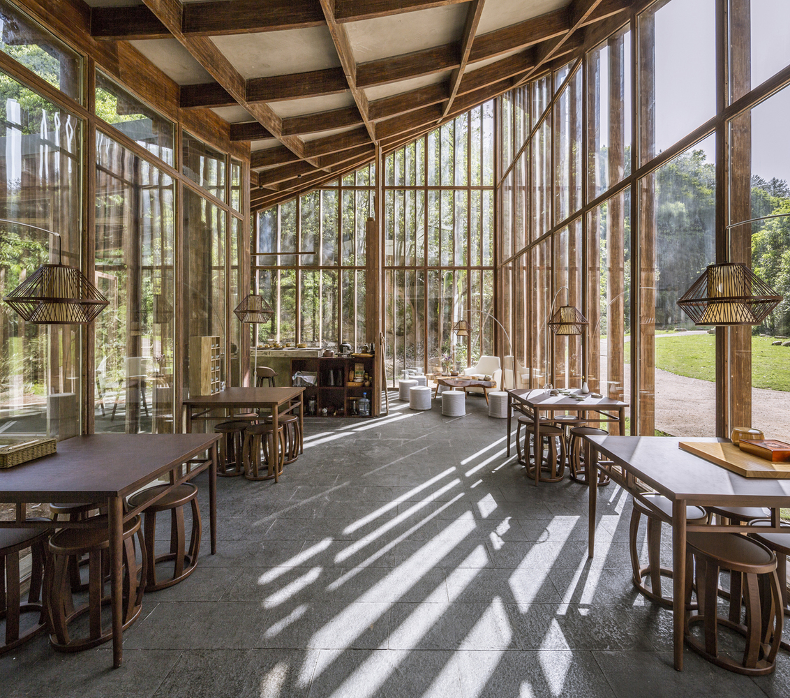 茶室东侧立面在布局上与接待堂东侧立面形成一条轴线,以求得在主要视点透视线上的连贯性。茶室的总面积为109平方米,是一个 “L”形的半围合院落,一端契入山体,另一端延伸并挑出到池塘上空。转折处的屋角约8米高,指向东南向的天空。这个“屋角”成为三条山谷会合处的空场的标识物,也成为和接待堂呼应的轴线上的制高点。屋面连续向两端陡降,形成一个狭长的内斜屋顶。立面通高的玻璃幕墙不仅带来了更宽阔的视觉体验,还给室内提供了充足的自然光线。