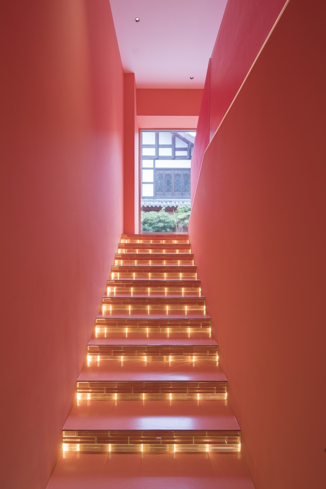 第一幕旨在铺陈。进入楼梯间,与寺庙正对的超大比例外凸窗将人的视线一直延伸至寺庙内建筑上,楼梯间墙、顶、地面的珊瑚珠红如寺庙围墙的延续,与寺庙产生对话。取景窗其实对内也对外:对室内定格一片墙景;对室外,在楼梯上行走的客人也构成了风景本身。第二幕旨在制造对立。 穿行在夹层走道,左右均为4.2m挑高空间,缓冲休息同时可俯瞰一层活动场景,以及欣赏专门为之预留挑高空间的装置。第三幕旨在事件如何结束,揭开伏笔,所有遗留未解的谜团都在此解开。