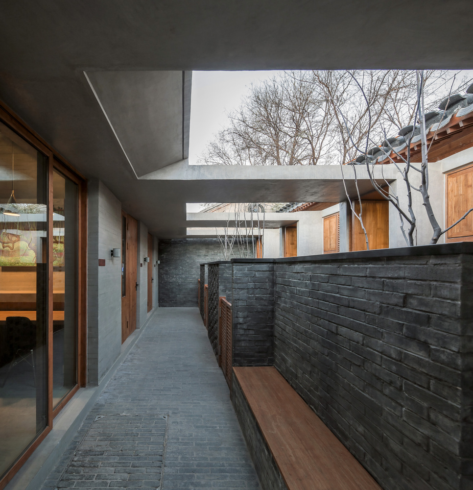 外人由喧闹的城市商业街区转折进入闲适宁静的胡同区域,经过大院胡同28号,先从老墙上的“三用”窗读到一丝新意,大门敞开,檐廊深远,绿意盎然,遂通过一条半室外主巷道进入,巷道上方覆盖混凝土顶板,与东邻西墙脱开缝隙,光线顺筐挤入照亮墙壁和甬道;走过北屋山墙,入第一进,才知此处既非杂院,也非独院,而是“宅园”社区;通过一条再次分支的巷廊,分别进入北侧、南侧不同格局和规模的五套“合院”公寓,每套公寓拥有大小、形状不同的小“合院”――园庭;园庭之中,麦冬草地围合,高树之下、低矮灌木之间,混凝土体块水平、竖直组合,既取意抽象的山石,又是室外坐具、内藏照明灯具、浇灌水喉,置于波形立瓦铺地之上,铺地可存薄水而成水中树石之景;由侧廊赏景而入户,主要起居空间通透,面向并对景于园庭――为“宅园合一”,使大院胡同28号的改造超出了原有的居住功能,向着“理想居所”靠近。