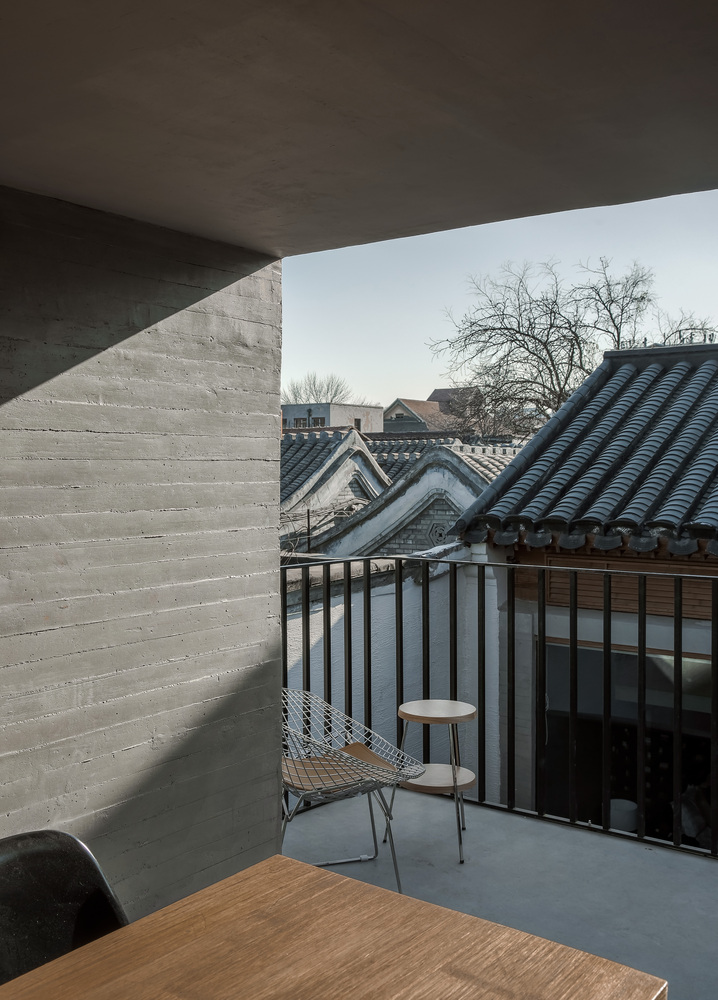 与主巷道串联的中屋最东侧公共空间单元,作为咖啡、餐茶空间,其坡顶局部抬高拉平,形成一个位于二层高度的半室外观景亭,嵌入原有建筑开间,其下压低为厨房操作空间。入口主巷道上方的混凝土檐板在此延伸为平台,与观景亭外侧连接为一体,在下限定出一个可休闲停留的户外灰空间,面对餐茶空间后部的公共小庭,在上的景亭“抬头”打破了原有瓦面坡屋顶的形态,视野在这里突然变得开阔,院落与城市景观交织,这也是公共巷道空间在剖面上的延伸。