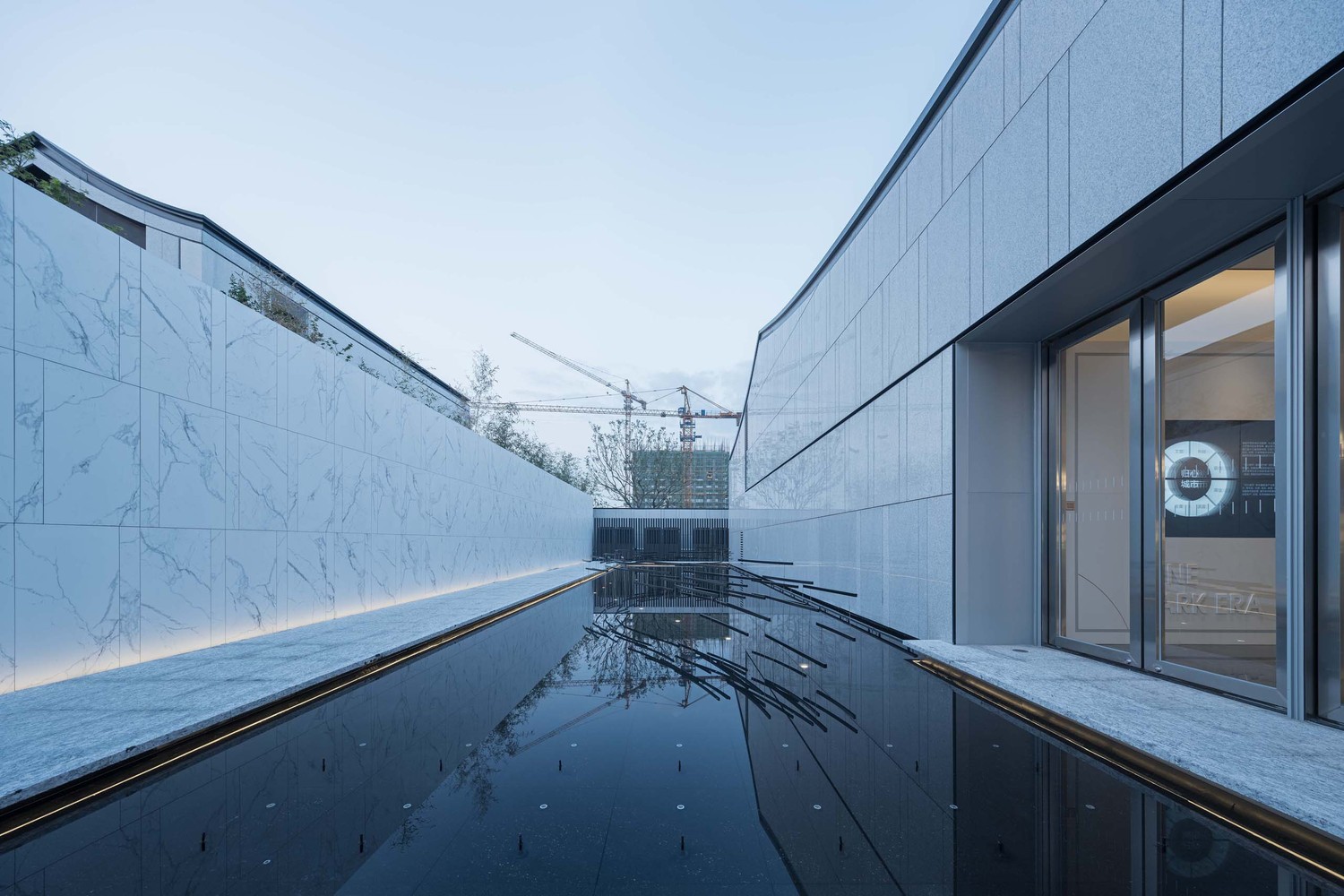 踏入前厅内,迎面即是景观中庭。自然光线透过中庭玻璃成为一处室内光源。四季更迭,光影变化,都像是被收集于这透明的景观容器内。与水景的结合,灌入这四方空间一股轻盈的流动感与鲜活的生命力,回应区域内临湖的环境特征