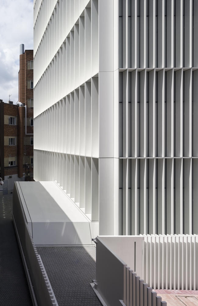 从形式上来看,由于整座建筑的体量非常有限,以至于其焦点都集中在幕墙立面形式上,在这种情况下,外立面密集的板条编织可以保护人们免受阳光直射以及来自周围建筑物的视线干扰。并通过玻璃上微妙的白色点状丝网得到加强,即使不用百叶窗,也能让室内获得更多的私密性,只有在一些异形的区域,如前厅与休息区,其延续性才会被打断,让位于通透的大玻璃窗,以证明室内的不同性质的空间。整座建筑的形象通过白色得到加强,与周边环境形成鲜明对比,呈现出一种朴素且无菌的形象。这一策略一直延续到地块的围栏处,目的是将建筑与医院的另一个同样由IDOM事务所设计的实验室大楼结合起来,在医院综合体内建立一个研究终端。