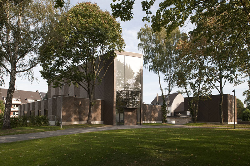 这座小巧简单的教堂独自矗立着,与外面的喧嚣形成对比。在小礼拜堂的后面,树丛环绕着一个新的骨灰龛。钟楼、教堂和礼拜堂的外立面均采用了斜向铺设的木板。这种简单的形式通过清晰的结构和真实的材质表现出来。