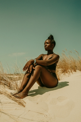 坐在沙丘上的非洲黑色泳衣女郎