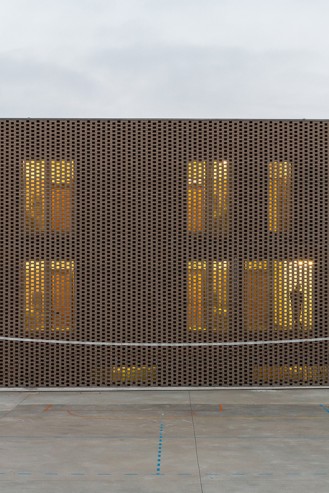 客户要求更多地使用自然通风,同时保留北向的入口,让运动场和建筑有更多的互动。建筑师选择使用渗透式的砌砖立面来满足建筑的自然通风和空气流动需求,为北向的房间提供自然采光,在保护窗户的同时,为通风装置提供了遮蔽。南向的室外的砖墙和室内围屏能有效地控制房间采光密度。