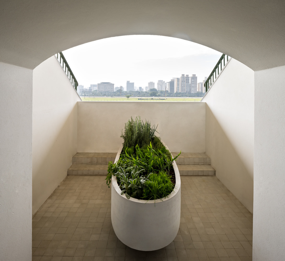 入口上方的天花板是高挑的,随后沿着长长的走廊降低下来。从平面上看,它有一个清晰的、由壁板和橱柜门形成的边界。凭借SCA这家巴西传统式厨房设计公司的技术,这些板件得以使用成薄片的大理石。位于中央的厨房岛台的有机形态,与房间严整的边界产生了冲突,这种冲突感又被从天花板引下的圆柱形油烟机所强化。自然光涌过走廊,平静地溢满这处空间,邀请着来者走向室外平台。站在那里,圣保罗摩天楼群的轮廓出现在人们眼前。