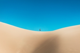 蓝天下行走在沙漠中的背包客