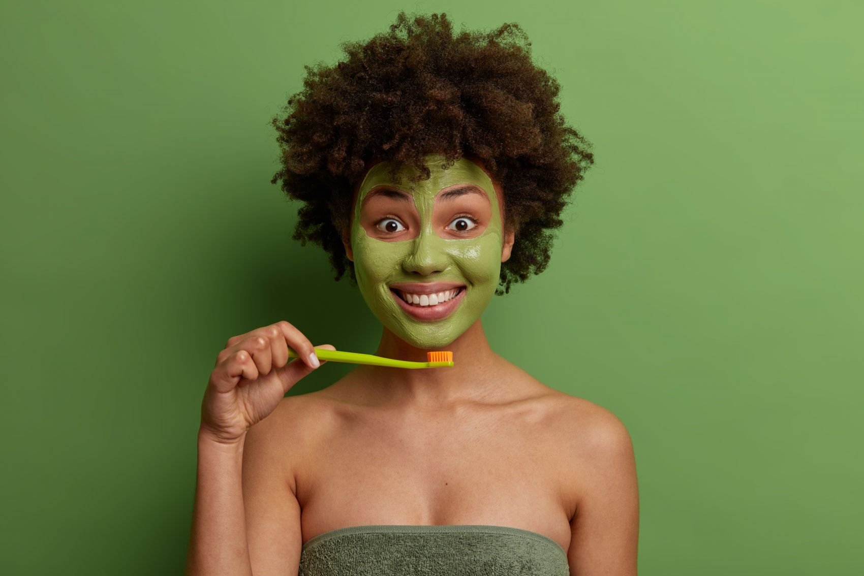 脸部涂满绿色硅藻泥面膜准备刷牙的非洲卷发女郎图片