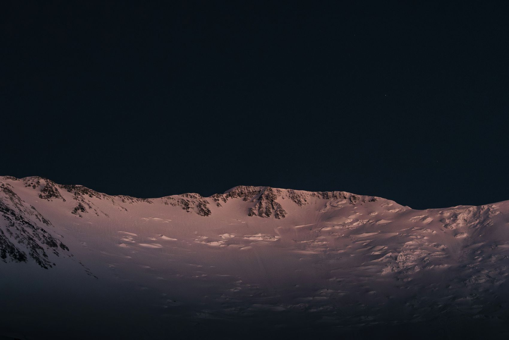夜雪山峦暮色特写:粉调光晕与深黑天幕的静谧雪山景观图片